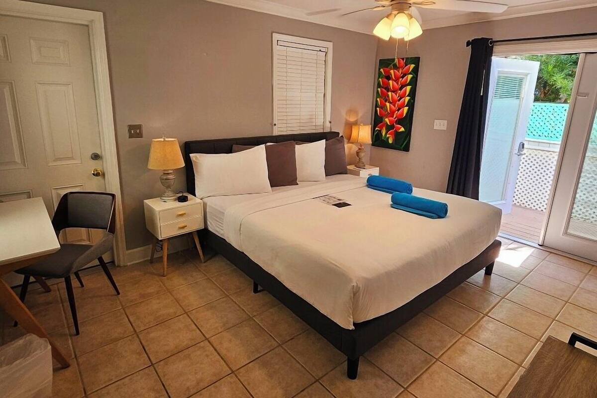 A hotel room with a bed, a desk, a chair, a ceiling fan, and a door.