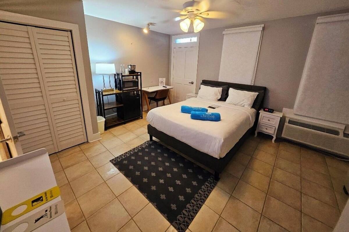A hotel room with a bed, a desk, a chair, a ceiling fan, and a window.