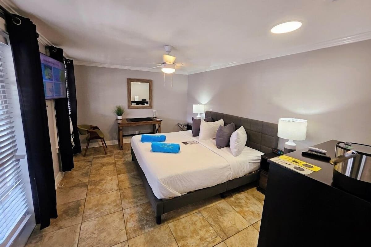A hotel room with a bed, bedside table, lamp, and a desk with a chair.