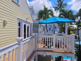 A wooden deck with a blue umbrella, white railings, and a pool area.