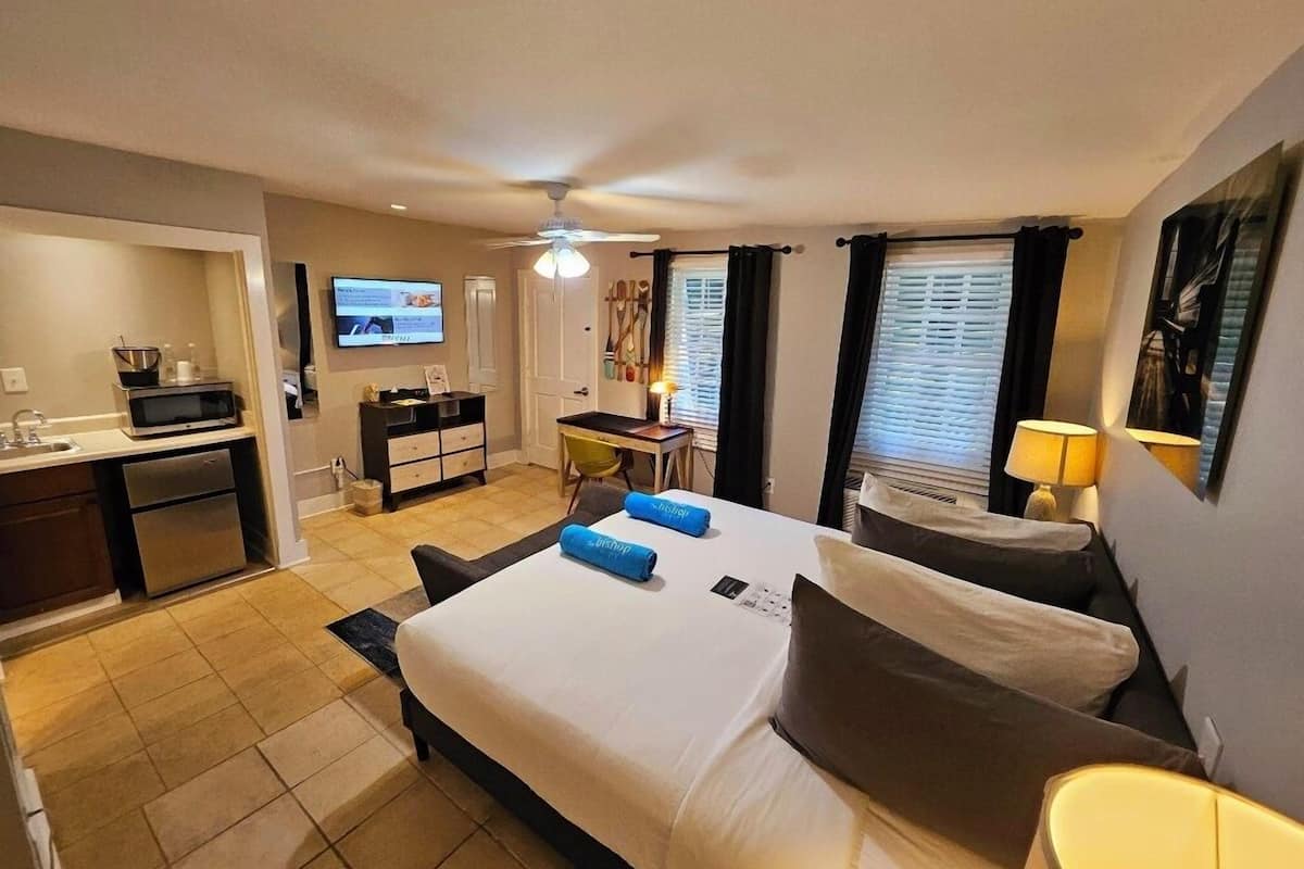 A hotel room with a bed, a desk, a TV, and a kitchenette.