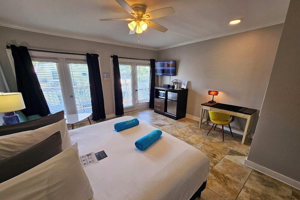 A hotel room with a bed, a desk, a chair, a TV, and a ceiling fan.