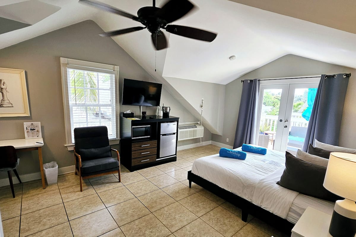 A bedroom with a bed, a desk, a chair, a TV, and a ceiling fan.