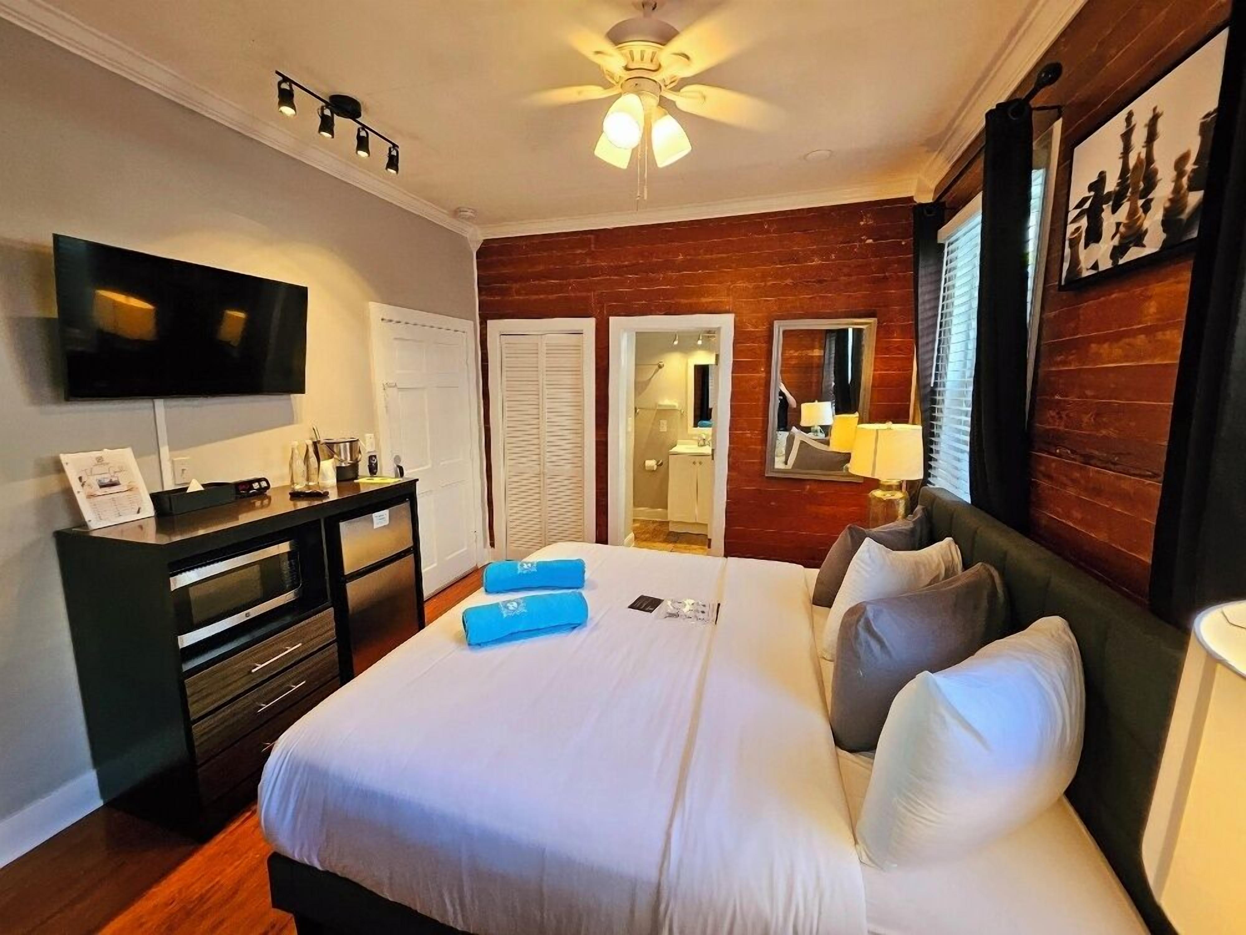 A hotel room with a bed, a desk, a TV, a ceiling fan, and a wooden wall.