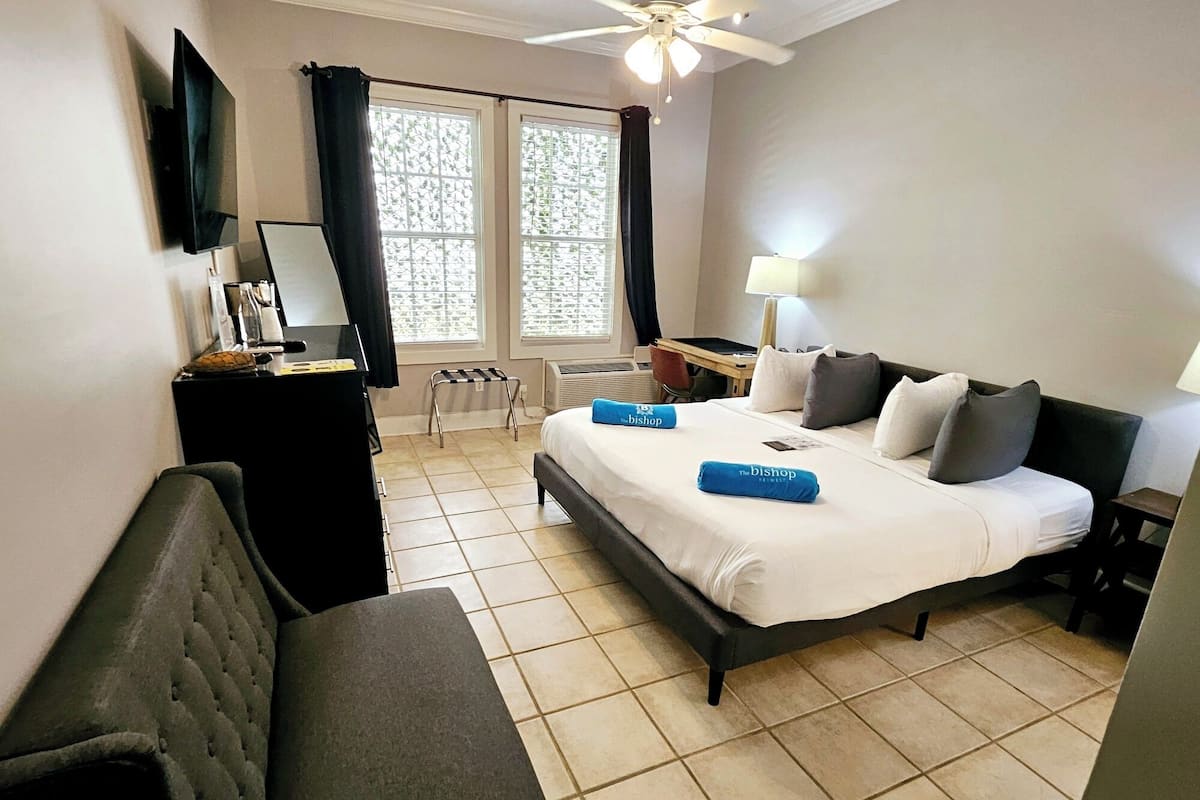 A hotel room with a large bed, a desk, a chair, a TV, and a window with curtains.