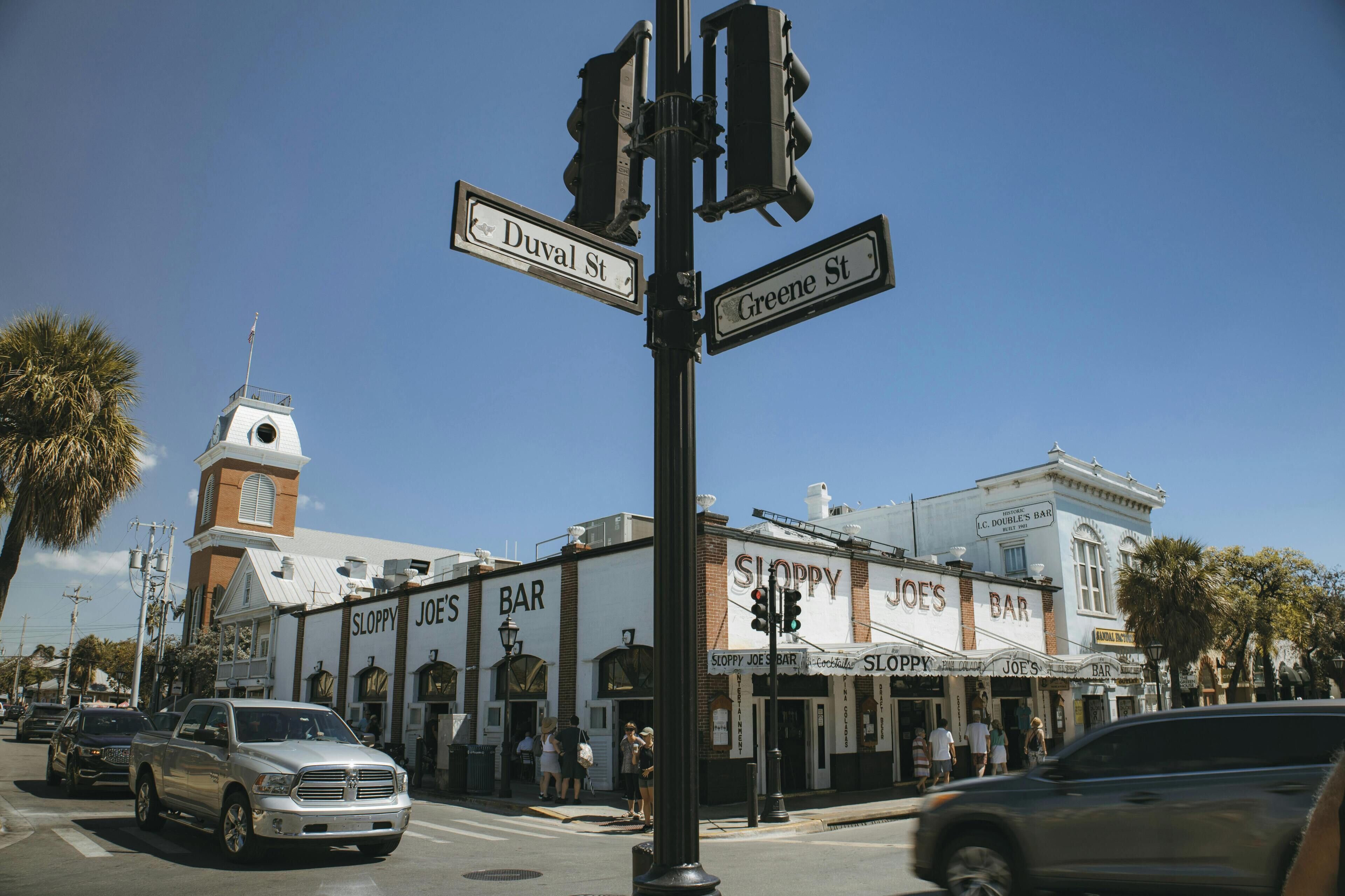 A street corner with street signs for Duval St and Greene St, a building with Sloppy Joe's Bar, and a church with a steeple.