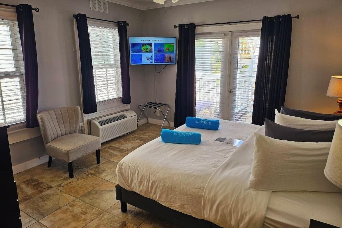 A hotel room with a bed, a chair, a TV, and a window with curtains.