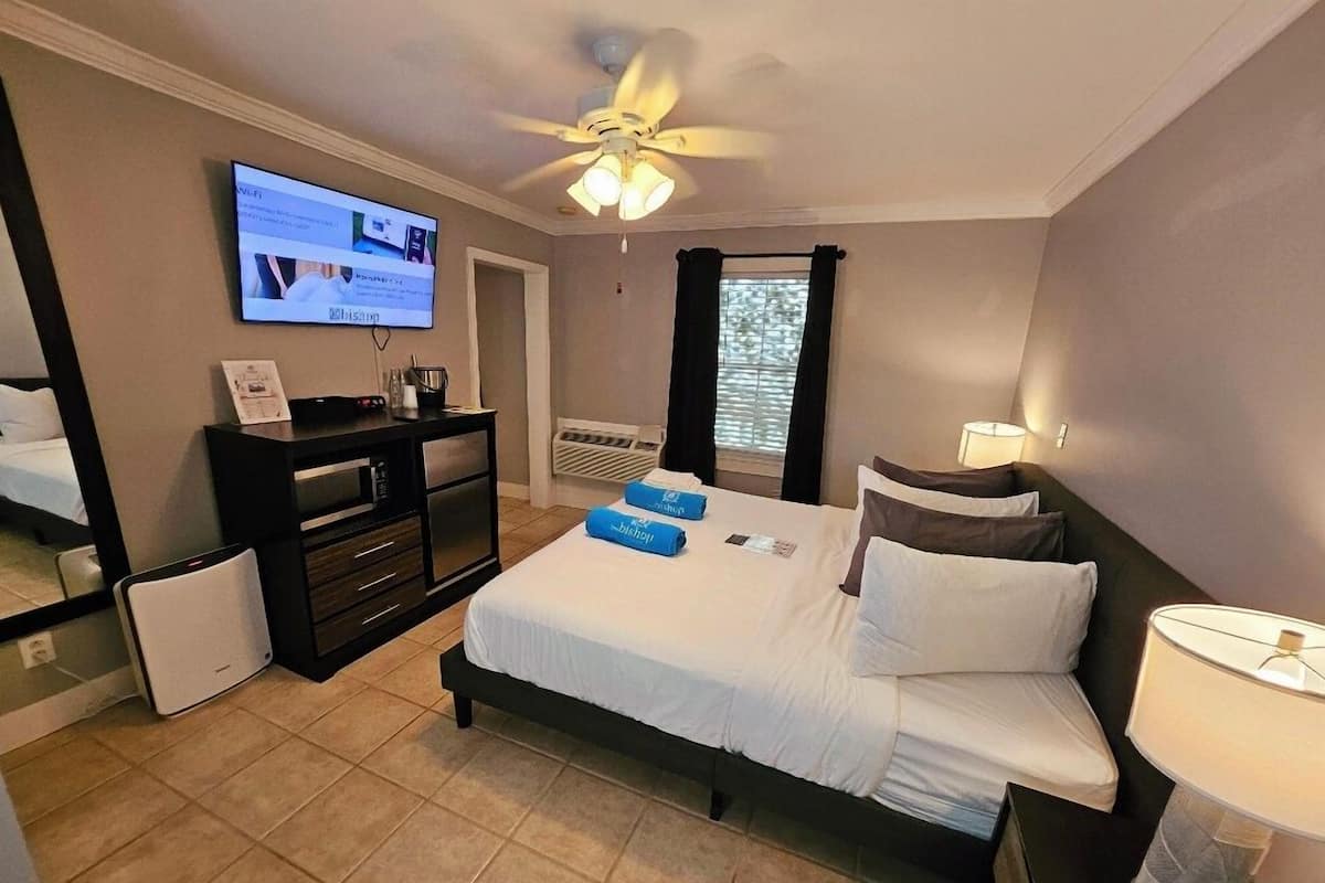 A hotel room with a bed, a desk, a TV, a ceiling fan, and a window with curtains.
