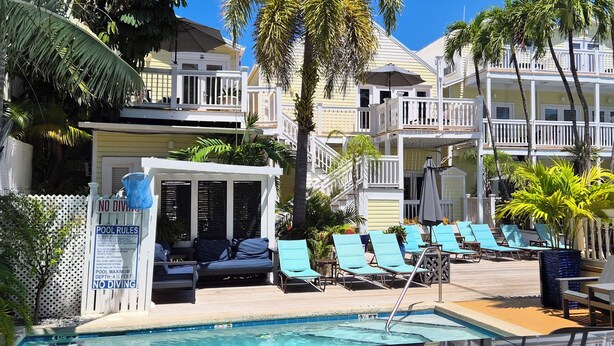 A pool area with lounge chairs, a pool with a depth limit sign, and a building with balconies. - Bishop Hotel Key West (Key West)