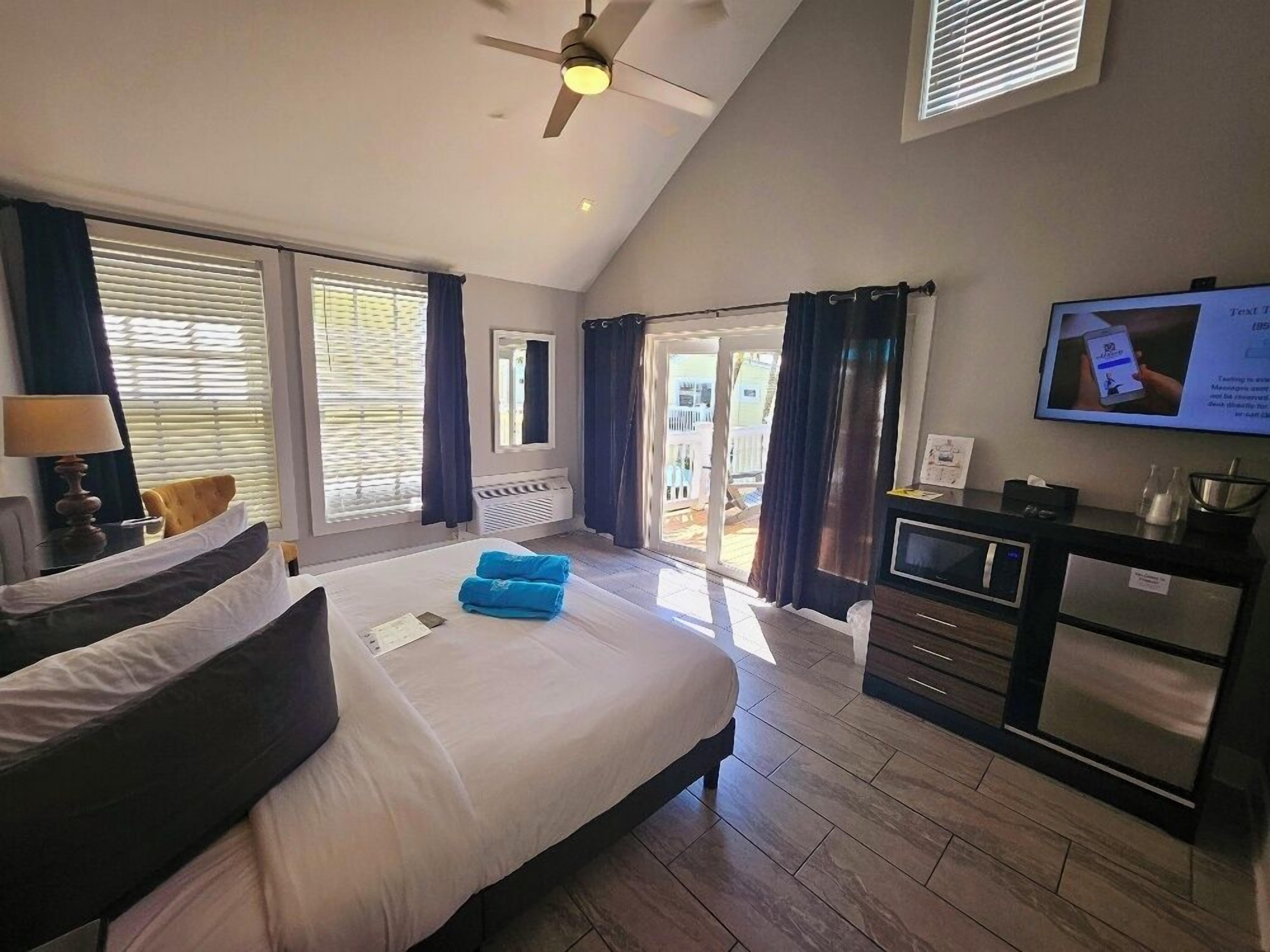A modern hotel room with a large bed, a desk with a computer, a TV, and a balcony with a view.