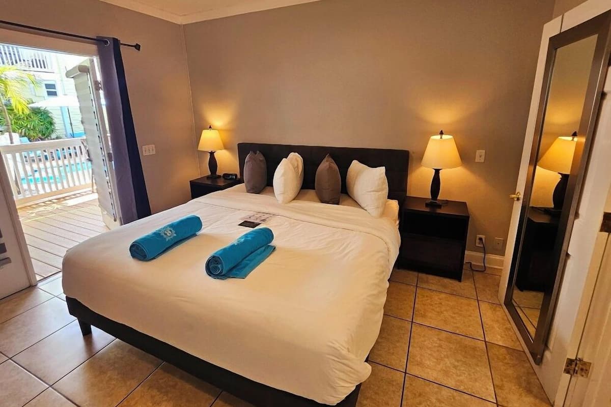 A hotel room with a large bed, two bedside tables with lamps, a door to a balcony, and a view of buildings outside.