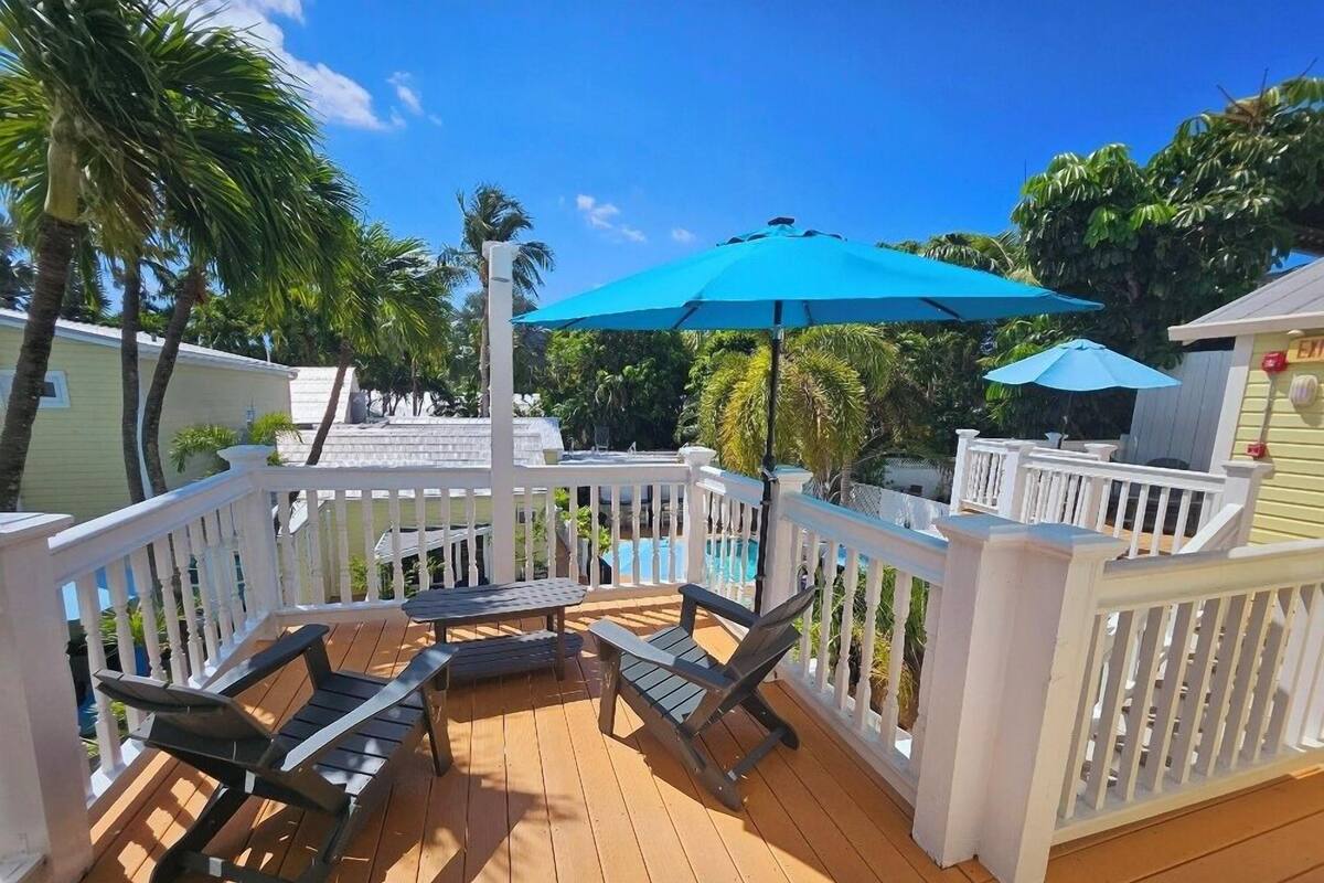 A wooden deck with a pool, white railings, and outdoor furniture.