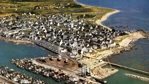 An aerial view of a coastal town with a marina, white houses, and a beach.
