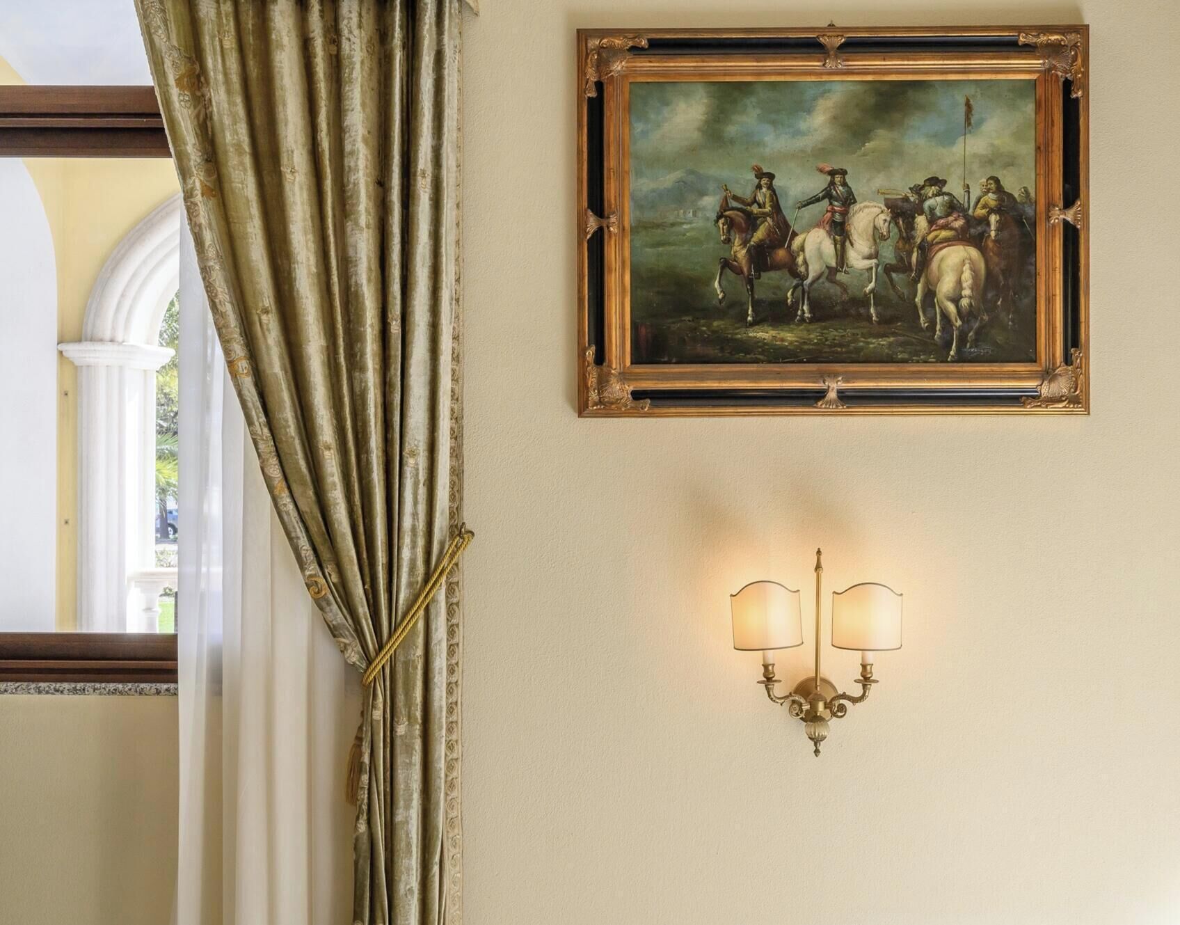 A wall with a framed historical painting and a wall-mounted light fixture.