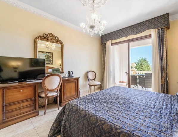 A hotel room with a bed, a desk, a television, a chair, a large mirror, and a view of the outdoors. - Hotiday Olbia Porto (Olbia)