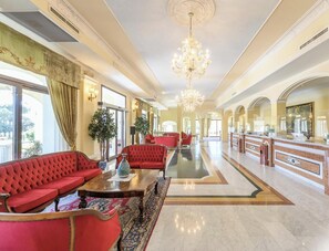 A spacious lobby with a grand chandelier, red upholstered seating, and a marble floor. - Hotiday Olbia Porto (Olbia)
