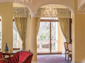 A spacious room with a large window, a chandelier, and a red chair. - Hotiday Olbia Porto (Olbia)