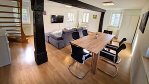 A modern living room with a wooden dining table, a grey sofa, and a staircase. - Zauberhaft Übernachten am EP (Ettenheim)