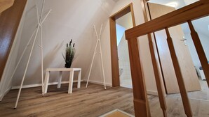 A room with a wooden floor, white walls, a small white table with a potted plant, and a wooden staircase. - Zauberhaft Übernachten am EP (Ettenheim)