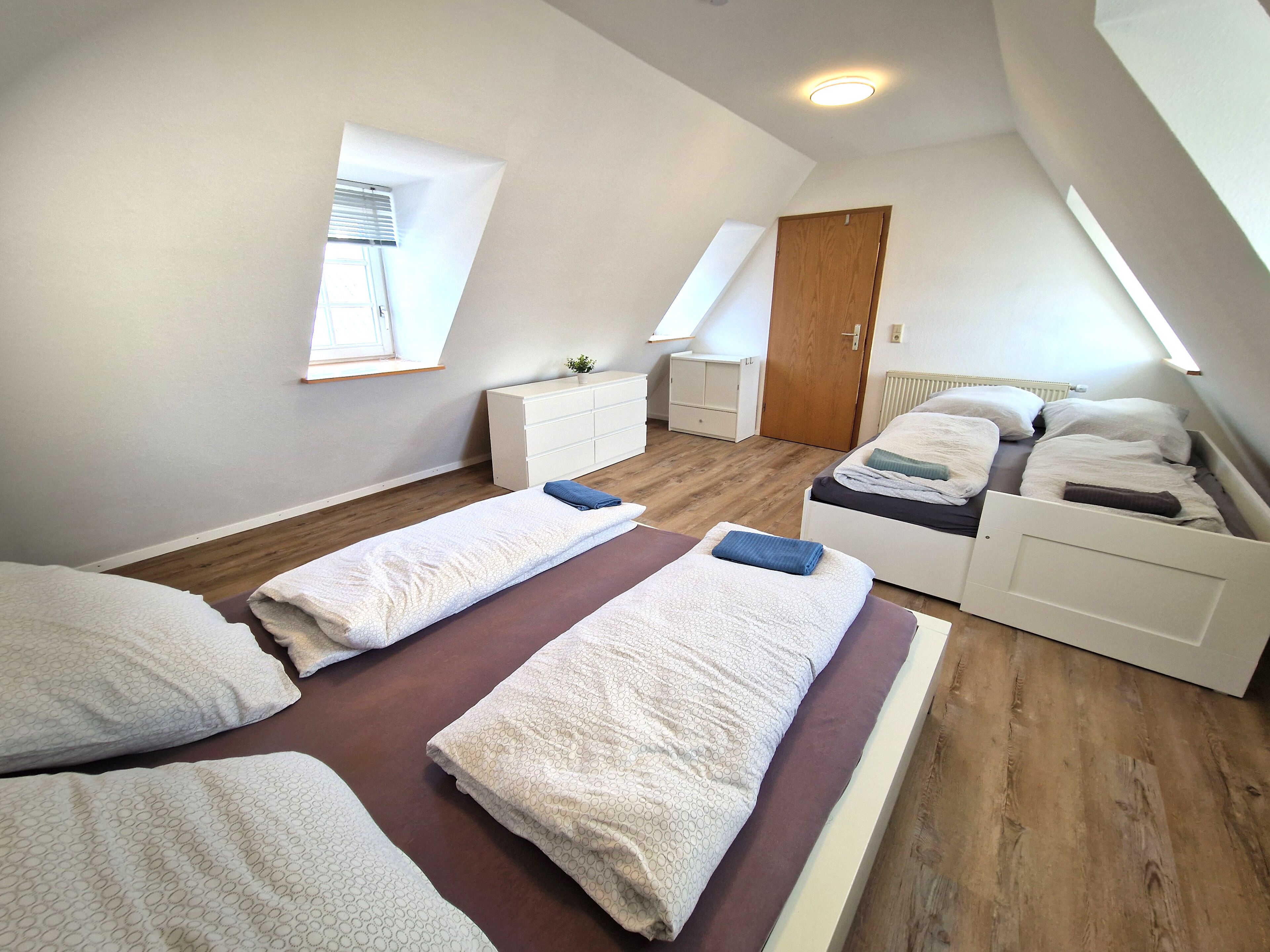 Une pièce moderne et bien éclairée, dotée d’un plafond en pente, d’un lit avec une tête de lit, d’une table de chevet, d’une commode, d’une fenêtre et d’une porte.