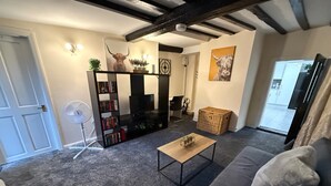 A living room with a dark grey carpet, a black bookshelf, a wooden coffee table, a grey sofa, and a white door. - Apartment - Sleeps 2 - Parking - Wifi (Colchester)