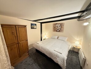 Um quarto com uma cama, duas luminárias de cabeceira, um guarda-roupa de madeira, um espelho e um quadro com o rosto de um leão na parede.