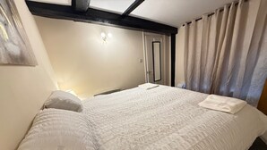 A neatly made bed with a textured white duvet and pillows, a bedside lamp, and a window with curtains. - Apartment - Sleeps 2 - Parking - Wifi (Colchester)