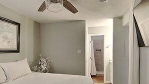 Une chambre à coucher avec un lit, un ventilateur de plafond, un tableau encadré au mur et une plante.