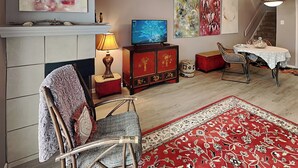 A living room with a fireplace, a television, a dining area with a table and chairs, and a staircase in the background. - Canvas Palms by Ryson Vacation Rentals (Galveston)