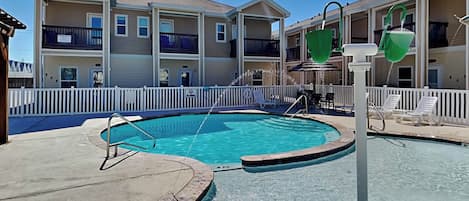 A swimming pool with a white fence and lounge chairs, surrounded by multi-story buildings with balconies.