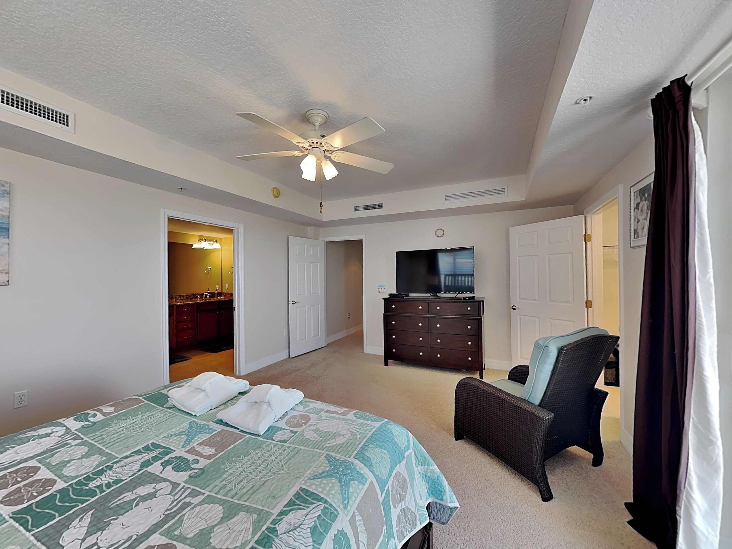 A bedroom with a bed, a dresser, a television, and a ceiling fan.