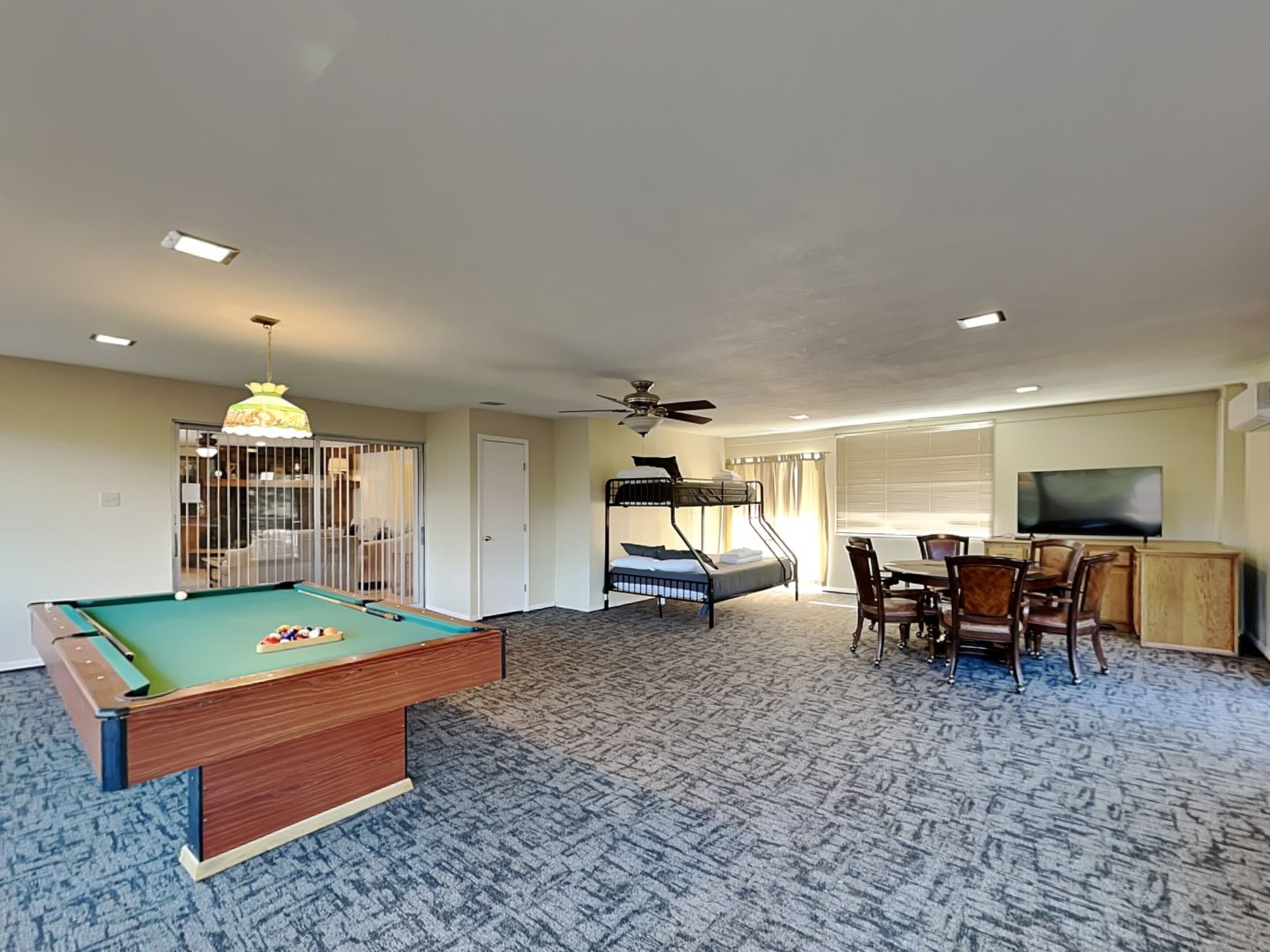 A room with a pool table, bunk beds, a dining area, and a TV.