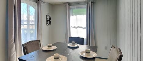 A dining area with a table set for four, a ceiling fan, and curtains on the windows.