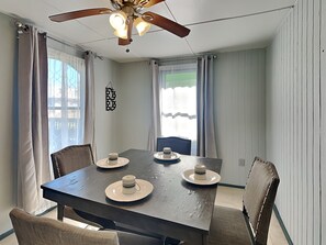 A dining area with a table set for four, a ceiling fan, and curtains on the windows. - Surfside Escape by Ryson Vacation Rentals (Freeport)