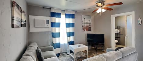 A living room with a grey sofa, a small white table, a TV, and a ceiling fan.
