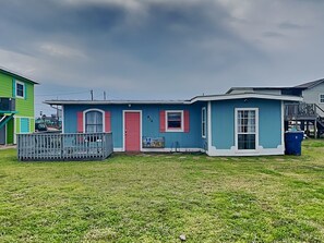 A single-story house with a front porch, a red door, and a small window. - Surfside Escape by Ryson Vacation Rentals (Freeport)