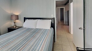 Una camera da letto con un letto, un comodino, una lampada e una porta che dà su un corridoio.