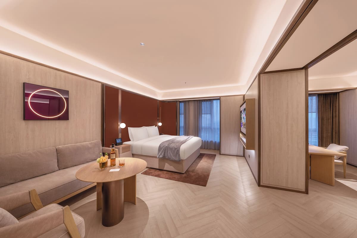 A modern hotel room with a bed, sofa, and a small table with a lamp.