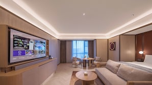 A modern hotel room with a large flat-screen TV, a sofa, a round coffee table, and a dining area with a table and chairs. - Crystal Orange Hotel Suqian Sucheng Government (Suqian)