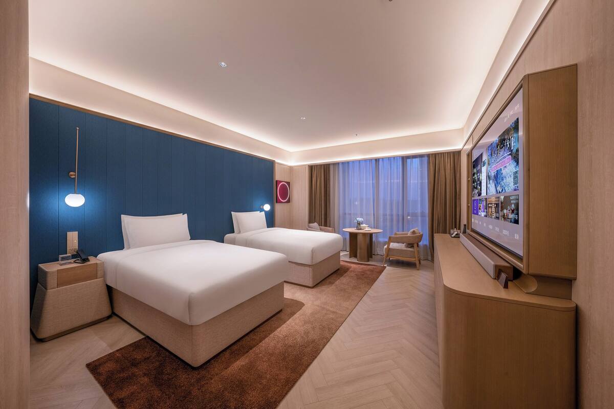 A hotel room with two beds, a TV, a desk, and a small table.
