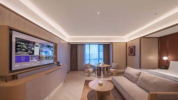 Een moderne hotelkamer met een grote flatscreen televisie, een bank, een ronde salontafel en een zithoek met een tafel en stoelen.