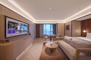 Una habitación de hotel moderna con un televisor de pantalla plana grande, un sofá, una mesa de centro redonda y un comedor con mesa y sillas.