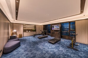 Habitación de hotel moderna con alfombra azul, equipo de ejercicio, televisión y vista a la ciudad.