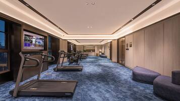 A fitness room with treadmills, stationary bikes, and a TV screen displaying workout videos.