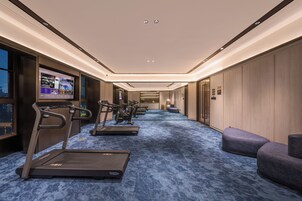 Un gimnasio con cintas de correr, bicicletas estáticas y una pantalla de televisión mostrando videos de ejercicios.