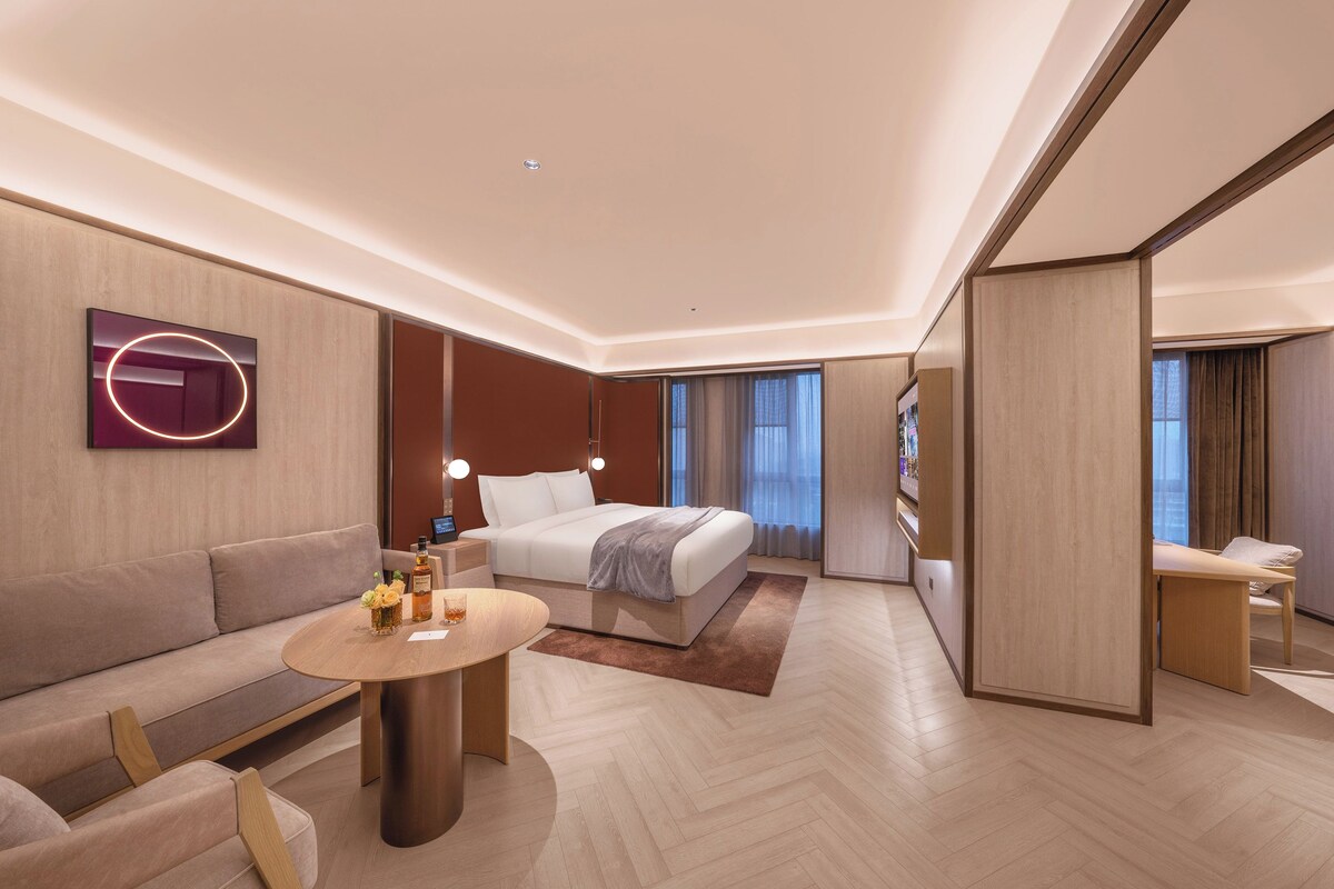 Una habitación de hotel moderna con cama, sofá y una pequeña mesa con lámpara.