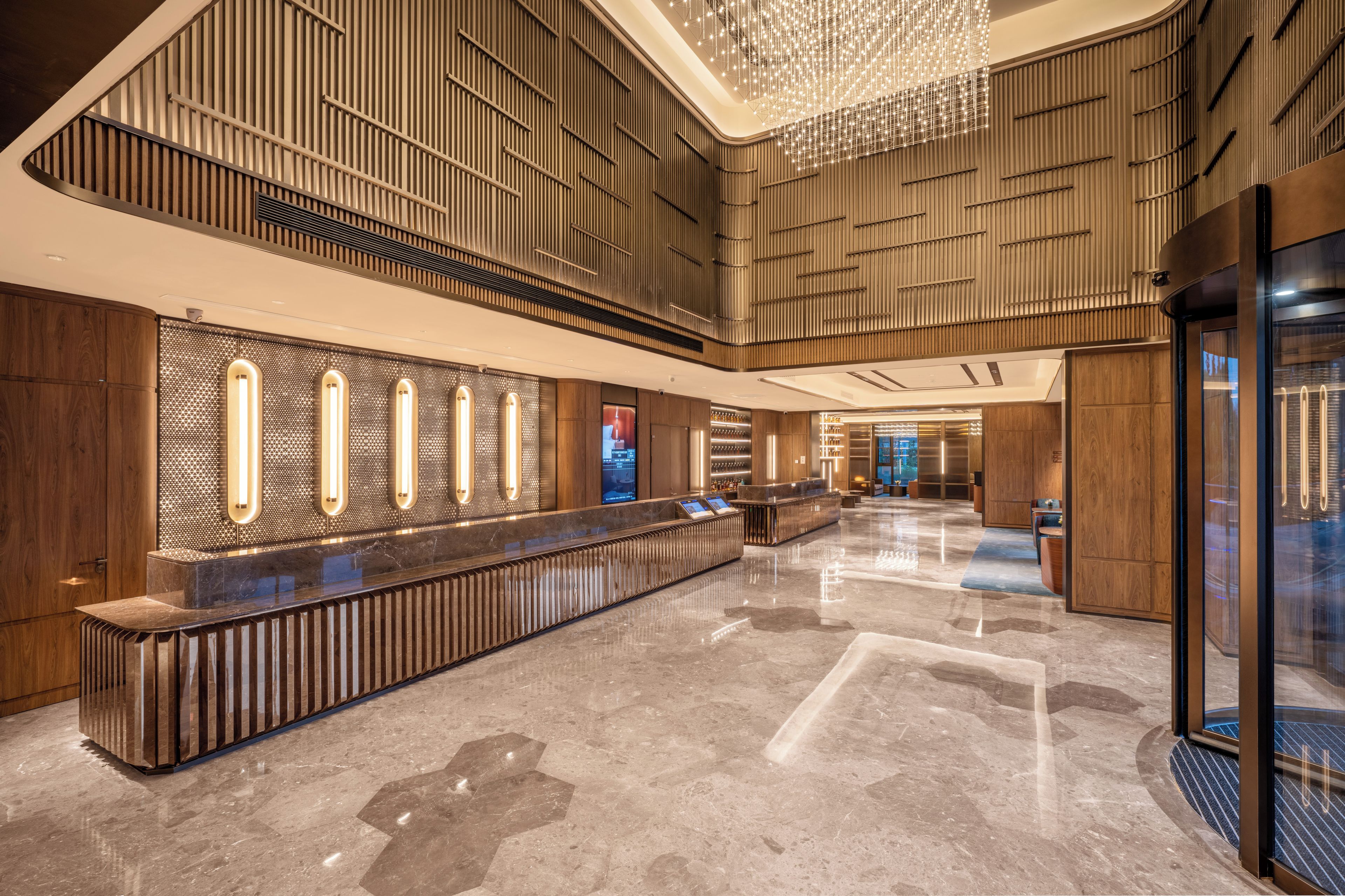 A spacious lobby with a long reception desk, wooden paneling on the walls, and a modern chandelier.