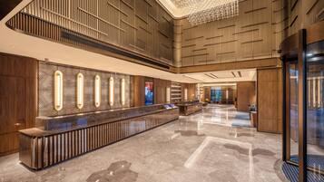 A spacious lobby with a long reception desk, wooden paneling on the walls, and a modern chandelier.