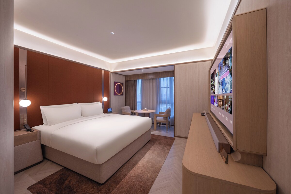 A modern hotel room with a large bed, a desk, a chair, and a television.