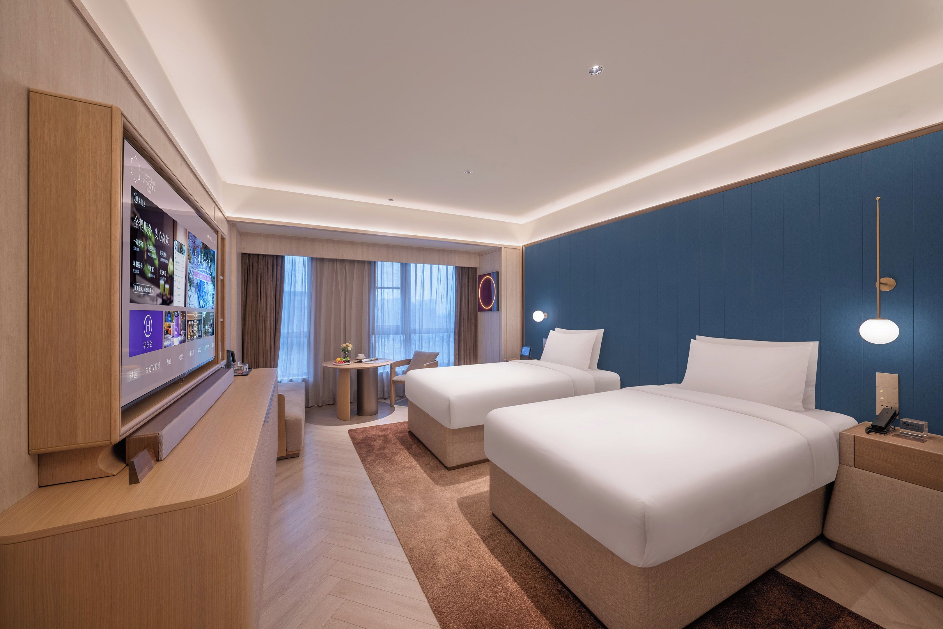 A hotel room with two beds, a desk, a TV, and a view of the outside.